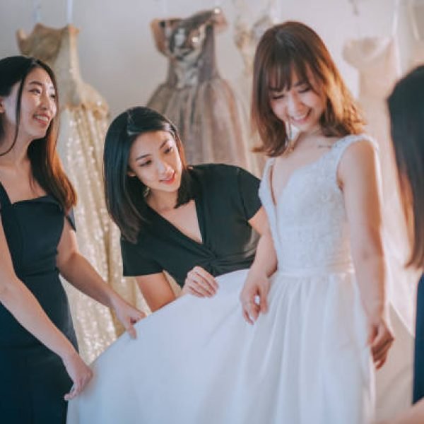 asian chinese bride trying on wedding dress surrounding by bridesmaid admiring examining the beauty of wedding gown at bridal shop